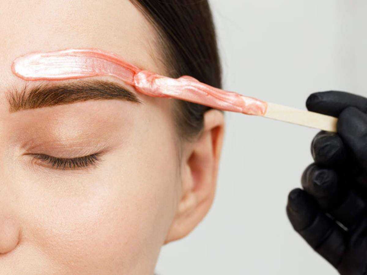 Eyebrow being shaped with pink wax applied by gloved hand.