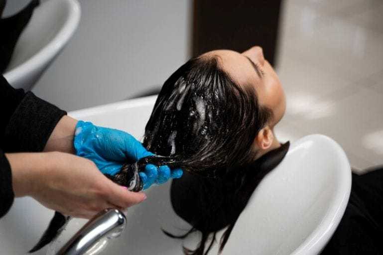 Person getting hair washed at a salon, gloved hands applying shampoo.